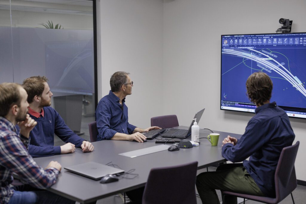 bildet viser fire menn rundt et bort som ser på en skjerm med illustasjoner